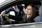 Side view of young beautiful woman sitting inside car and holding hand on steering wheel. She smiling and talking with