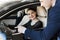 Side view of young beautiful woman sitting inside car and holding hand on steering wheel. She smiling and talking with