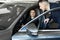 Side view of young beautiful woman sitting inside car and holding hand on steering wheel. She smiling and talking with