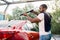 Side view of young black man in casual clothes, car wash employee or auto owner, washing luxury red car under high