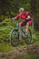 Side view of young caucasian male jumping with a mountain bike over a jump on a singletrail. Epic ride with a modern mountain bike