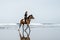 side view of young female equestrian riding horse on sandy