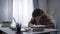 Side view of young genius in eyeglasses typing on laptop keyboard and writing in workbook. Portrait of absorbed