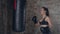 Side view of young girl in black boxing gloves training technique with punching bag