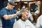 Side view of a young handsome man visiting barbershop and getting new trendy haircut. Barber working with hair clipper