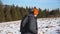 Side view of young hiker with backpack and stick in hand climbing on snowy hill in field. Sporty guy hiking on snow