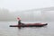 Side view of young kayaker in river, padding, man enjoying water sport in foggy morning with bridge on background, male rowing