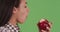 Side view of a young Latina eating an apple on green screen
