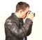 Side view from a young man with a leather jacket holding a vintage camera making a photo - Isolated.