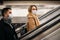 Side view of young man and woman in medical masks on escalator in subway.