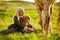 Side view of young mother with little girl in dresses embracing spotty horse on green meadow