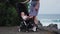 Side view of young mother pushing baby stroller over summer beach background