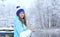 Side view of young smiling woman with a cup of hot tea or coffee on snowy winter waterside.