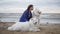 Side view of a young woman sitting on the sand and embracing her dogs of the Samoyed breed by the sea. White fluffy pets