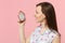 Side view of young woman in summer clothes holding half of fresh ripe pitahaya, dragon fruit isolated on pink pastel