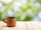 Side of vintage brown baked clay coffee cup on wooden table with natural light bokeh from sunlight between green leaf