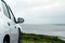 Side of a white car parked with view on beautiful ocean scene. Travel and rent vehicle concept