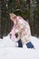 Sider view of youthful girl in winterwear rolling snowball in winter forest