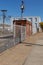 Sidewalk alongside a commercial industrial facility, newer chain link fence and barbed wire, power poles with heavy cable lines