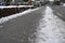 Sidewalk covered with a wet dirty snow. On the both sides there are layers of snow cleared away as winter maintenance.