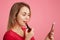 Sideways portrait of female lady paints lips with red lipstick, uses smart phone as mirror, prepares for date with handsome man, a