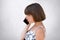 Sideways portrait of little girl with bobbed hair, wearing white dress, speaking over cell phone with serious expression. Stylish