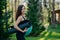 Sideways shot of beautiful slim woman with perfect figure, wavy dark hair, holds rolled up karemat and fitness ball, poses outdoor
