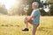 Sideways shot of healthy elderly male stretches legs, has serious expression, wears sport clothes and shoes, stands against nature