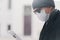 Sideways shot of man in hat, sunglasses and protective mask, reads newspaper outdoor, poses at street, finds out news from press