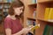 Sideways shot of serious college female student focused in book, poses in school library, chooses necessary literature for