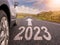 Sign 2023 and directional arrow on small asphalt country road and a side of a car. Travel and explore concept. Warm sunny day, sun