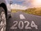 Sign 2023 and directional arrow on small asphalt country road and a side of a car. Travel and explore concept. Warm sunny day, sun