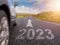 Sign 2023 on small asphalt country road and and arrow and side of a car in motion blur. Travel and explore concept. Warm sunny day