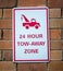 Sign hanging on brick wall with text 24 HOUR TOW-AWAY ZONE and picture of tow truck