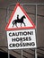 Sign hanging on gate with picture of horse rider and words CAUTION! HORSES CROSSING