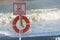 Sign with inscription in Russian `It is forbidden to swim in stormy weather` against the backdrop of large waves and life buoy. Fo