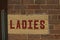 Sign painted on a brick wall reading ladies