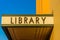 A sign for a public library in green lettering on a yellow corrugated iron marquee
