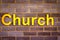 Sign reading Church in large, bold yellow capital letters on a brick wall