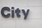 A sign that says, City, in gray illuminated letters on the front facade of a business with a large arch shaped window