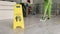 Sign showing warning of caution wet floor and worker cleaning hall floor of business building.