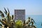 Sign stating `No Swimming!` in 8 languages is nestled amongst ornamental agave plants along the Sea of Galilee