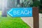 Signpost beach, made of wood, green, the road to the beach to the left, on the background of the road and the green plants of the