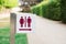 Signpost for men's and women's restrooms in park near trimmed tall green bush