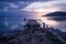 Sihouettes of people along pier with orange sunset on purple blue sky along lake Itza, El Remate, Peten, Guatemala