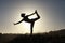 Silhouette of acrobatic teen gymnast balancing with the sun behind