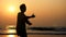 Silhouette of active senior woman practicing tai chi gymnastic on sandy beach.