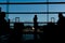 Silhouette of airline passengers in an airport lounge at the wide observation window watching an airplane flying of