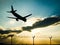 Silhouette of airplane landing in sunset to the airport behind barbed wire fence