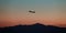 Silhouette of an airplane soaring through the sky in front of a stunning backdrop of mountains.